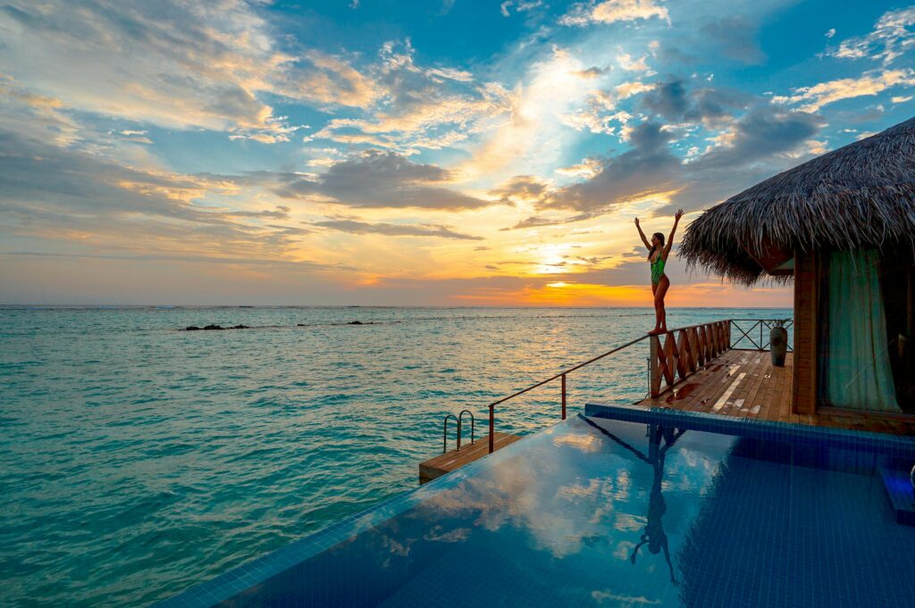 Woman enjoying a stunning sunset at a luxury Maldives resort's infinity pool.