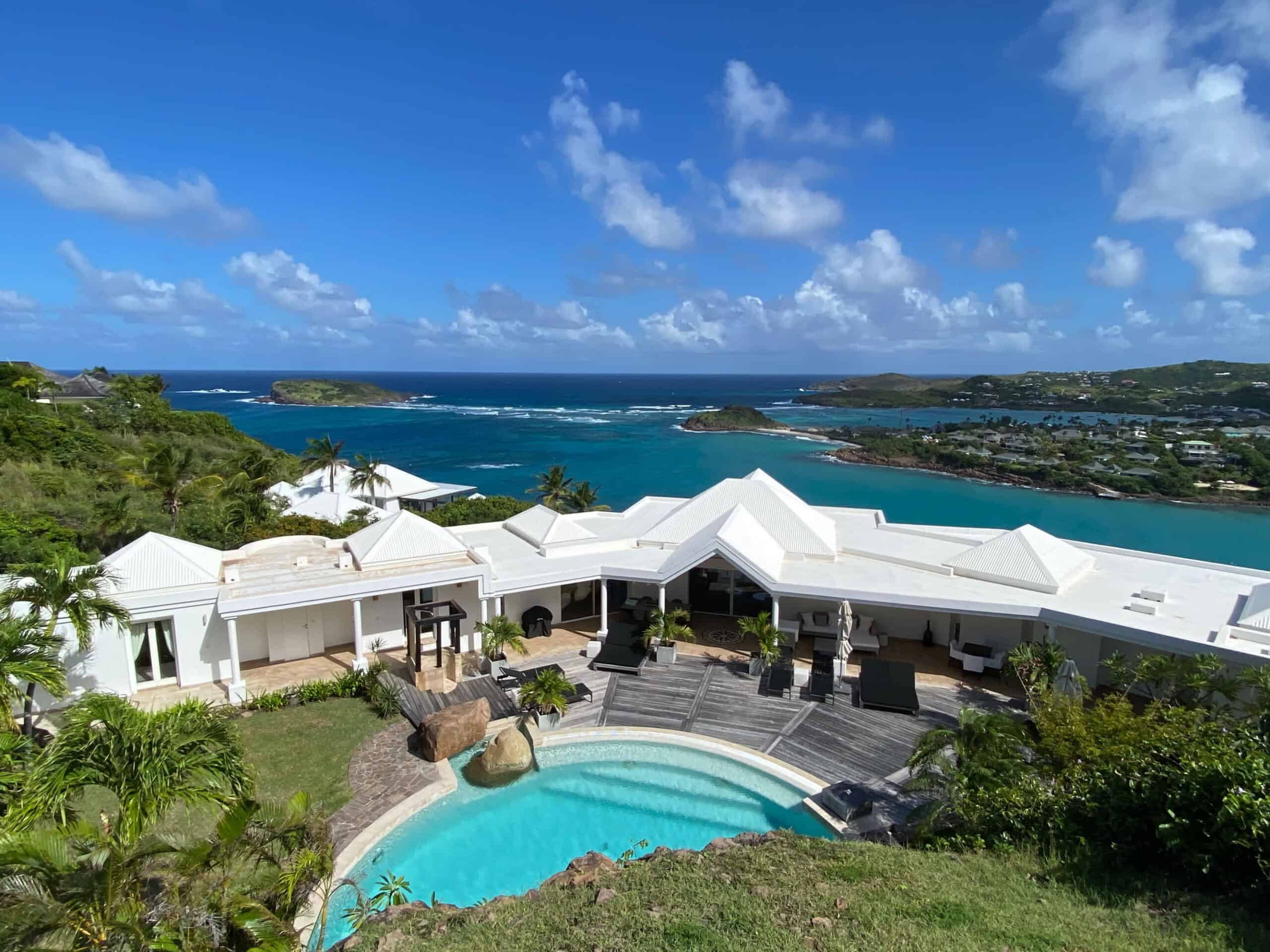 A serene hillside villa overlooking a turquoise bay, where white rooftops gleam under the sun and a private pool invites endless relaxation amid lush greenery.