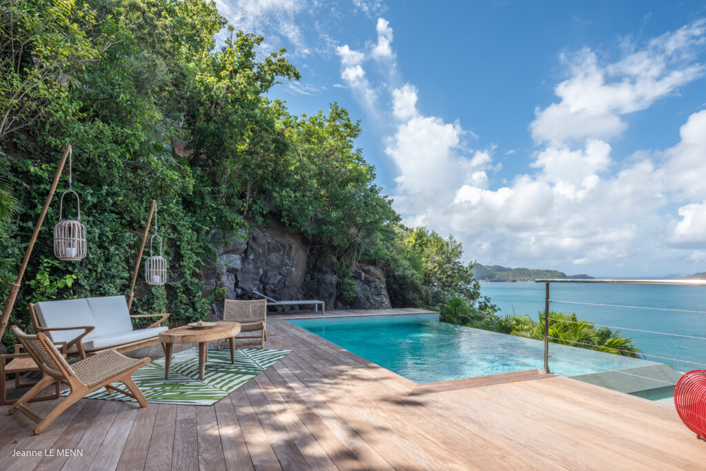 A luxurious eco-friendly villa in St. Barts featuring a wooden deck, infinity pool, and sustainable bamboo furniture, blending seamlessly with lush greenery and overlooking the turquoise Caribbean Sea. The design reflects the island's commitment to sustainable living while offering breathtaking ocean views in a serene natural setting.