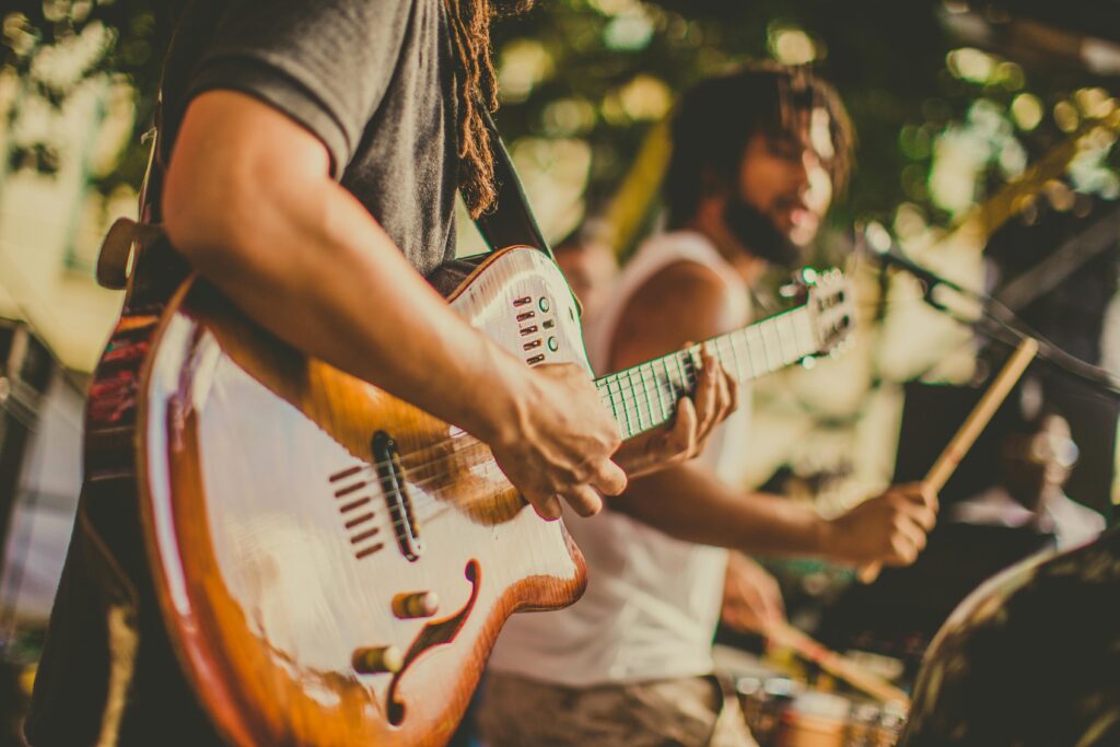 A lively musical performance in St. Barts, featuring a close-up of a guitarist strumming a beautifully crafted wooden guitar, with a drummer energetically playing in the background. The warm tones and dynamic movement capture the island’s vibrant music scene, blending Caribbean rhythms with soulful melodies in an open-air setting.