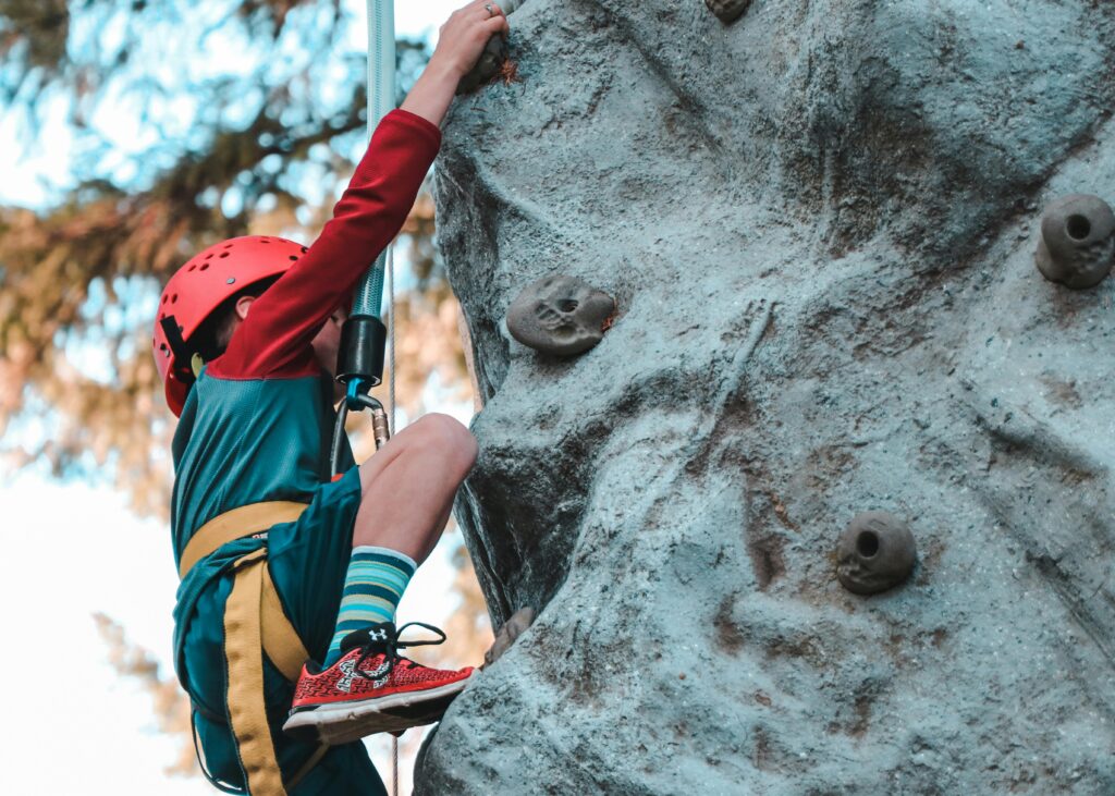 A young adventurer in a red helmet and harness rock climbing in St. Barts. The island offers thrilling outdoor activities beyond its beaches, including climbing experiences that challenge both kids and adults against a scenic tropical backdrop.