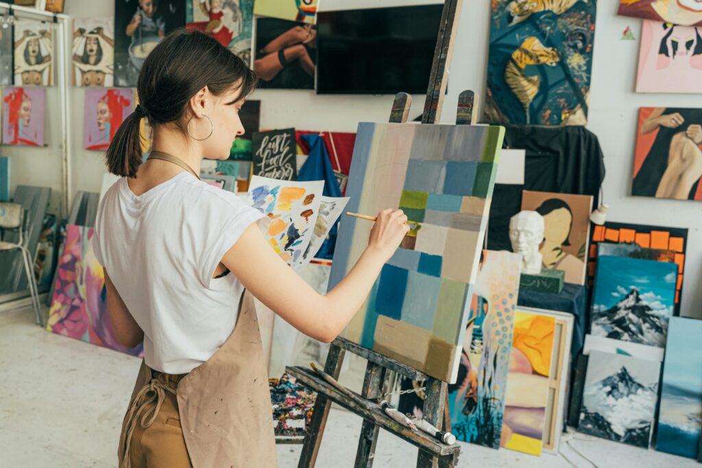 female artist painting an abstract piece in a vibrant studio filled with colorful artworks, representing the thriving arts and design scene in St. Barts, where creativity flourishes through local and international artistic expressions.