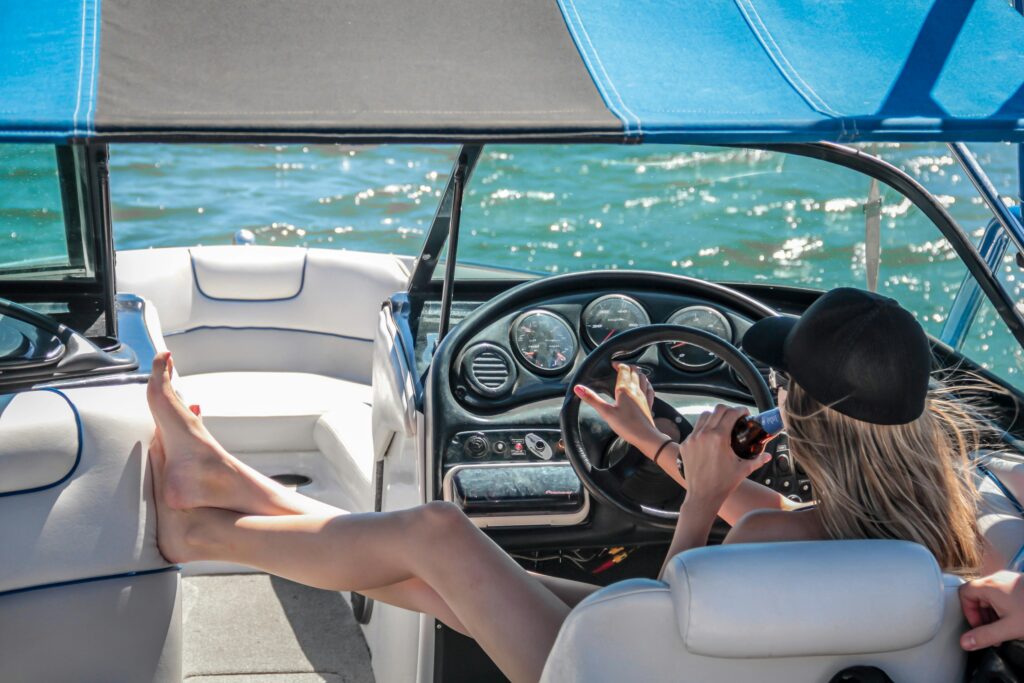 A woman relaxing on a luxurious yacht in St. Barts, steering with one hand while sipping a drink, enjoying the sun and sea breeze. This scene captures the essence of a celebrity getaway, blending leisure and exclusivity in a tropical paradise.